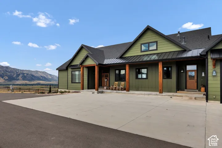 Modern farmhouse exterior featuring board-and-batten siding, heavy timber porch posts, metal roofing accents, a concrete driveway, and mountain scenery