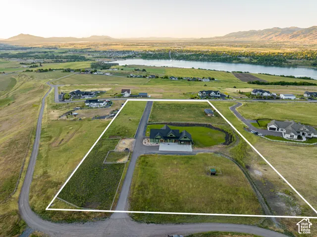 Aerial perspective of a multi-acre property featuring a large residence, expansive open grounds, a paved driveway, and mountain scenery