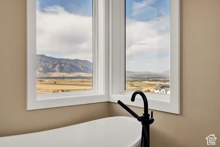 Freestanding white soaking tub with a matte black floor-mounted faucet, positioned before corner windows capturing mountain and valley scenery