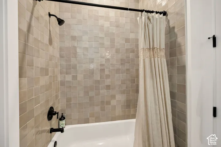 Bathtub enclosure featuring matte black hardware, wall-mounted shower head, and neutral-toned square tile surround
