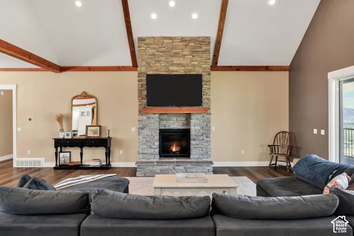 Vaulted ceilings with exposed beams, floor-to-ceiling stone fireplace, wood-finish flooring, and recessed lighting
