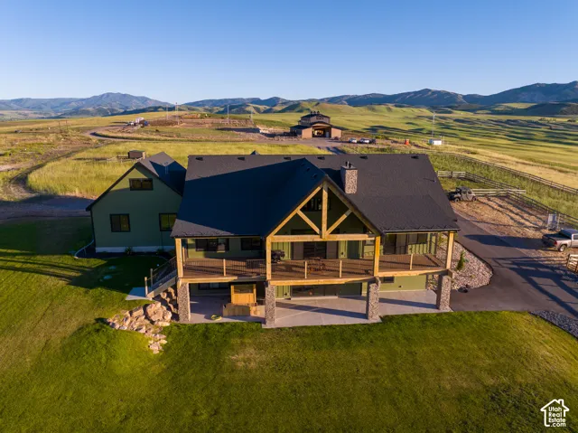 Multi-level exterior featuring timber framing, stone-clad support pillars, an expansive elevated deck, and a lower-level concrete patio set against a mountain backdrop