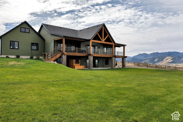Multi-level residence featuring lap siding, an expansive elevated deck with timber-frame trusses, stone column bases, and a mountain backdrop