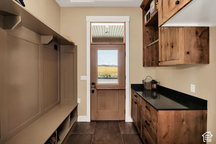 Custom wood-finish cabinetry, built-in storage bench with overhead shelving, dark stone-finish countertops, and a wood-frame exterior door with a transom window