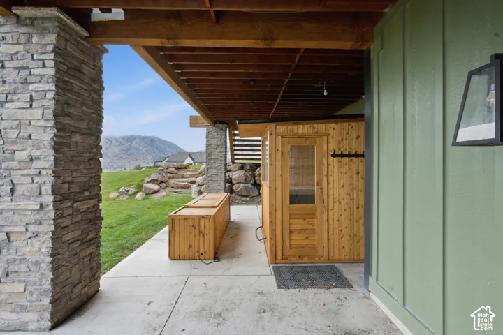 Covered patio featuring stacked stone pillar supports, wood-paneled sauna, board-and-batten siding, and mountain backdrop