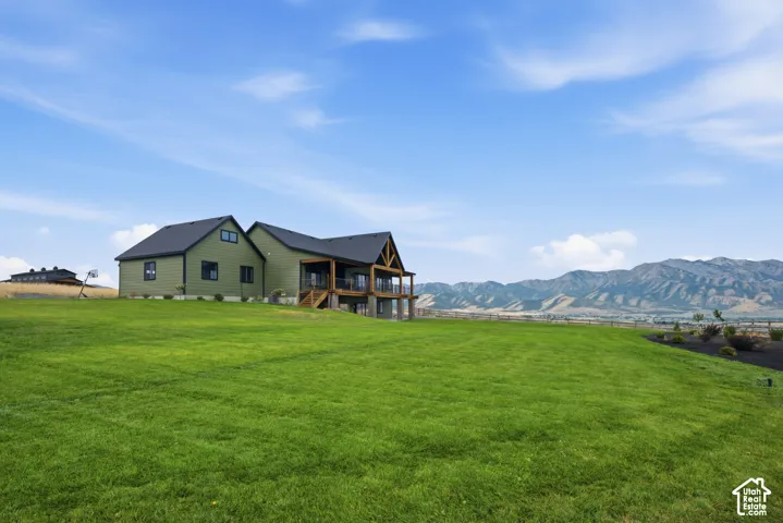 Exterior featuring horizontal siding, a gabled roofline, a raised wooden deck with timber framing, and expansive grounds set against a mountain backdrop