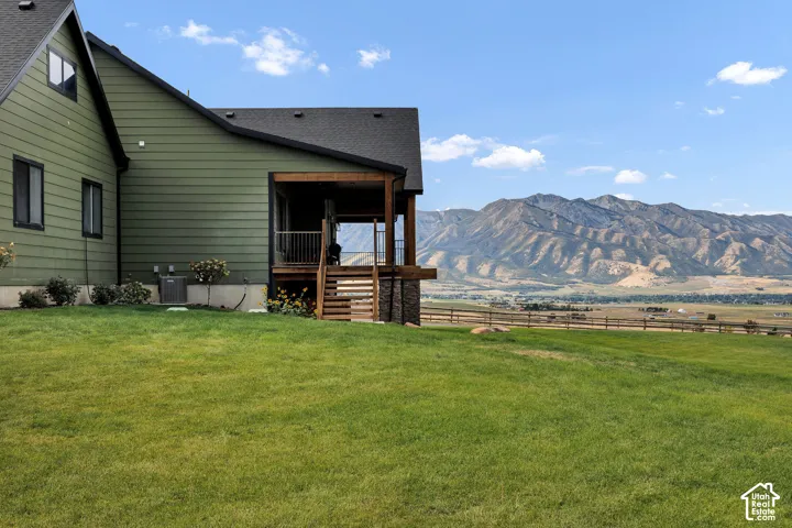 Exterior siding with wood-finish accents, covered deck with stairs, stone foundation detailing, expansive lawn, and mountain backdrop