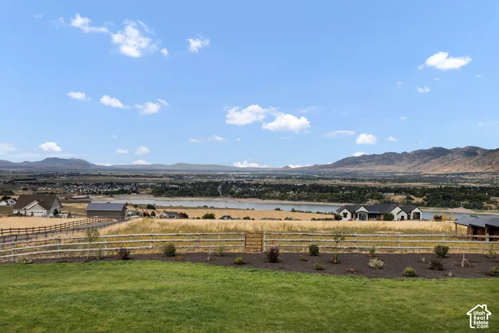 Expansive mountain and lake landscape featuring a manicured lawn, dark mulch garden beds, and split-rail perimeter fencing