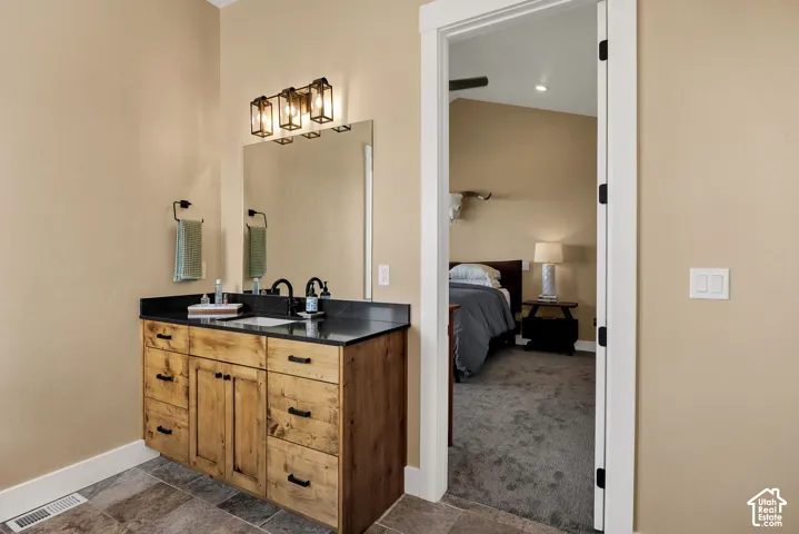 Vanity featuring a natural-finish wood cabinet, dark stone countertop, undermount sink, and matte black hardware, accented by a three-light wall-mounted fixture and large rectangular mirror