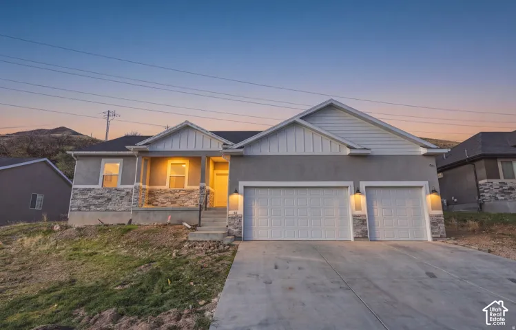 Single-story exterior featuring a concrete driveway, two-car garage, natural stone veneer accents, and board-and-batten siding