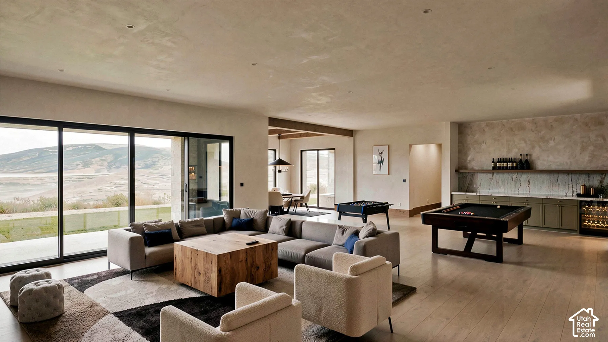 Expansive open-concept living area featuring wood-finish flooring, floor-to-ceiling sliding glass doors, textured wall finishes, and a built-in wet bar with stone backsplash and custom cabinetry