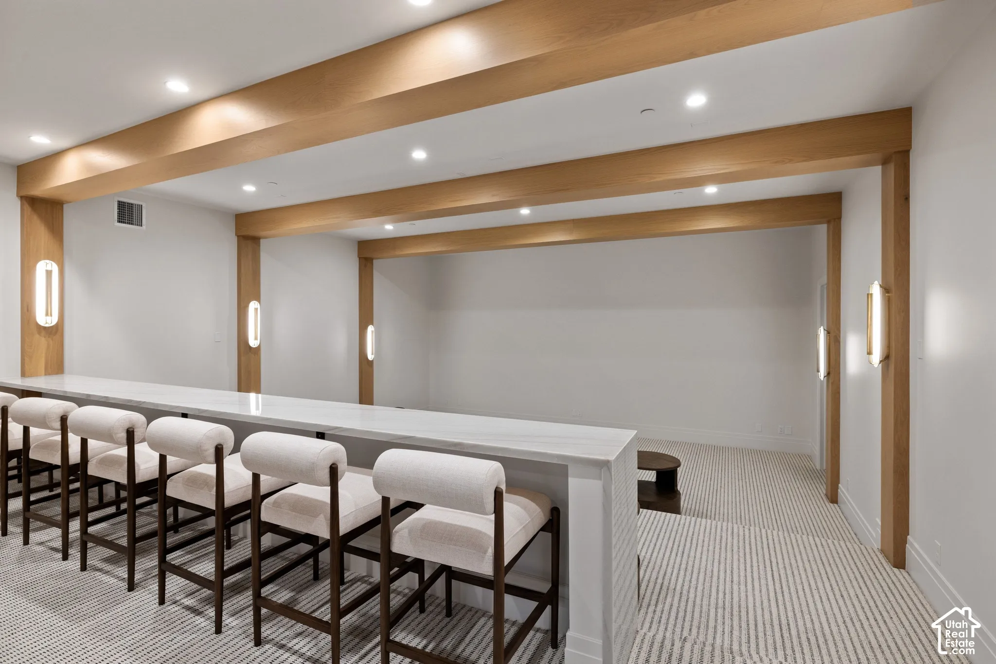 Custom built-in tiered bar with a stone countertop, recessed ceiling lighting, structural natural wood beams, and vertical wall-mounted sconces