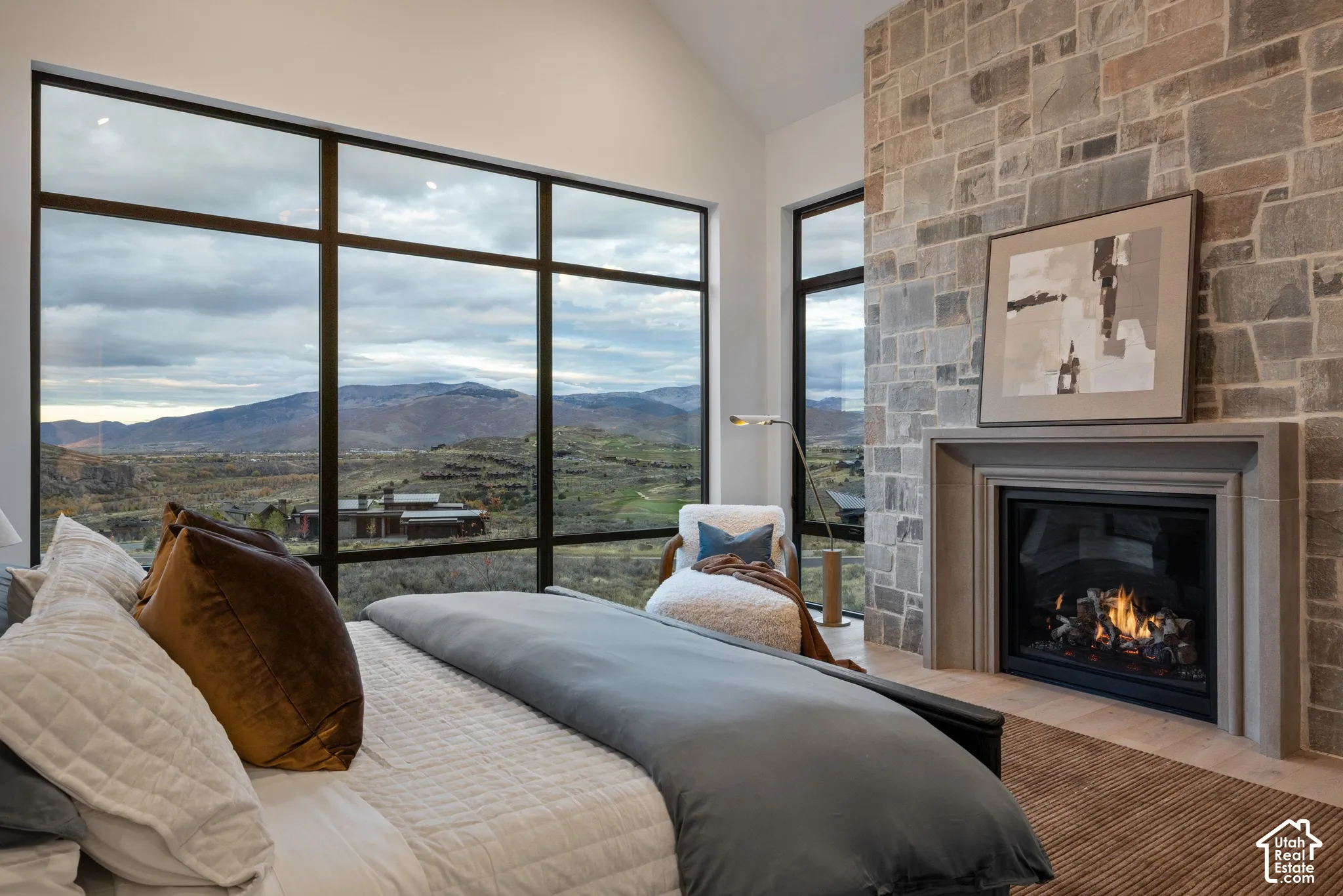 Vaulted ceiling, floor-to-ceiling multi-pane windows, mountain scenery, and stone-surround fireplace with a tailored mantel
