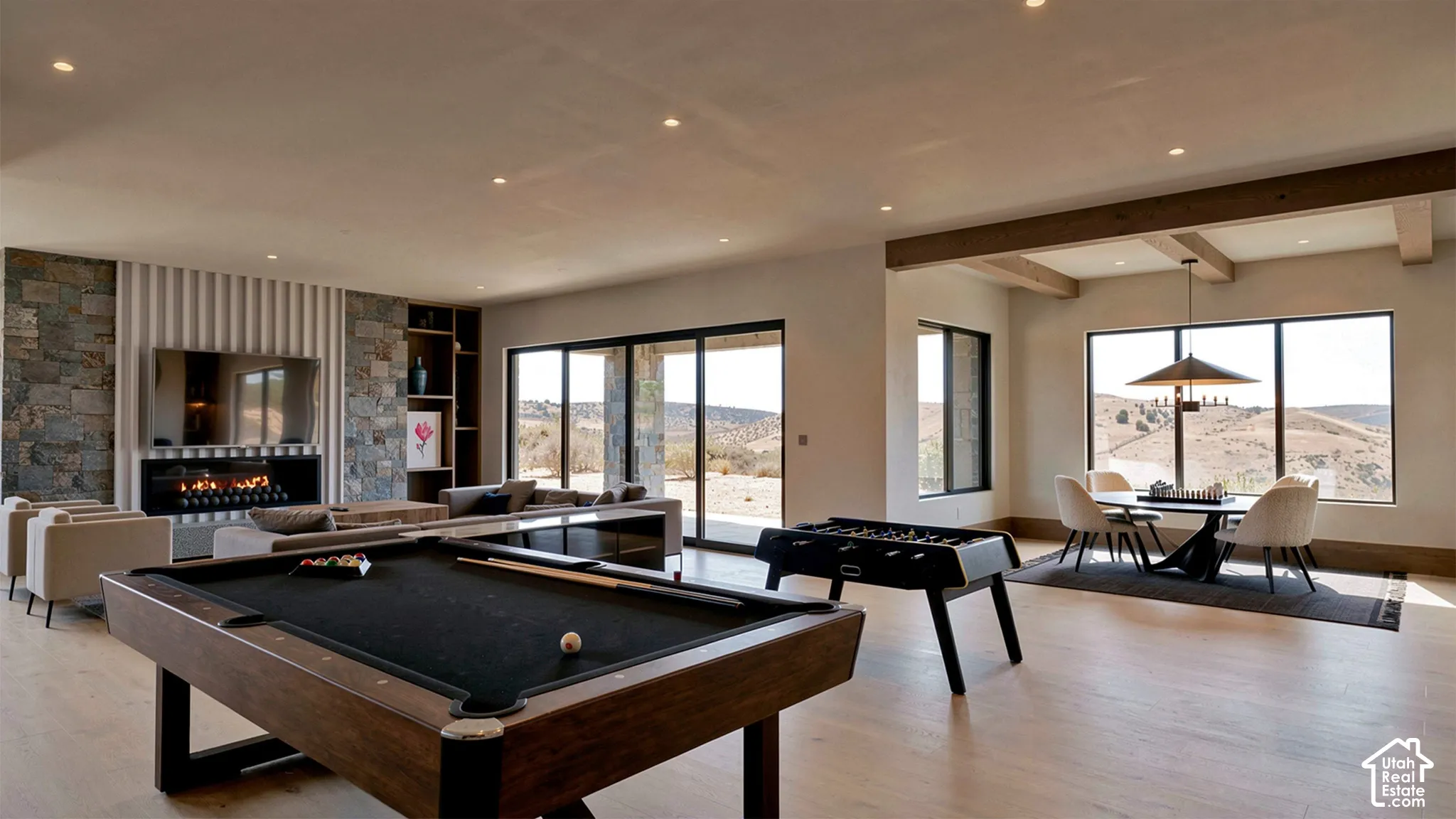 Open-concept living space featuring wood-finish flooring, a linear fireplace with stone masonry surround, recessed lighting, exposed ceiling beams, and large sliding glass doors