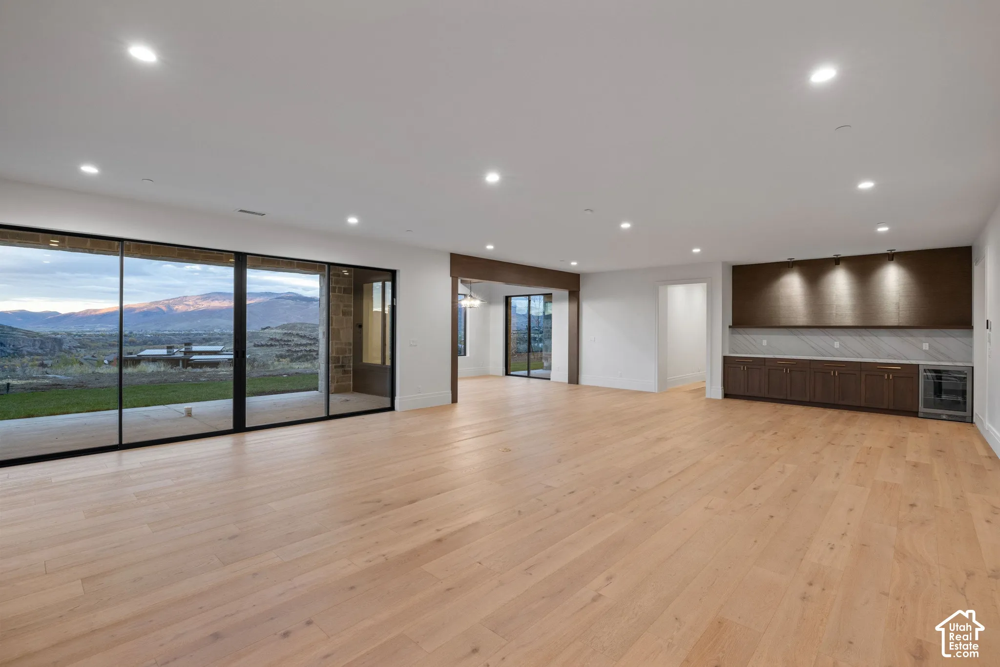 Open floor plan featuring wood-finish flooring, recessed lighting, built-in cabinetry with a beverage refrigerator, stone-style backsplash, and floor-to-ceiling glass sliding doors with mountain scenery