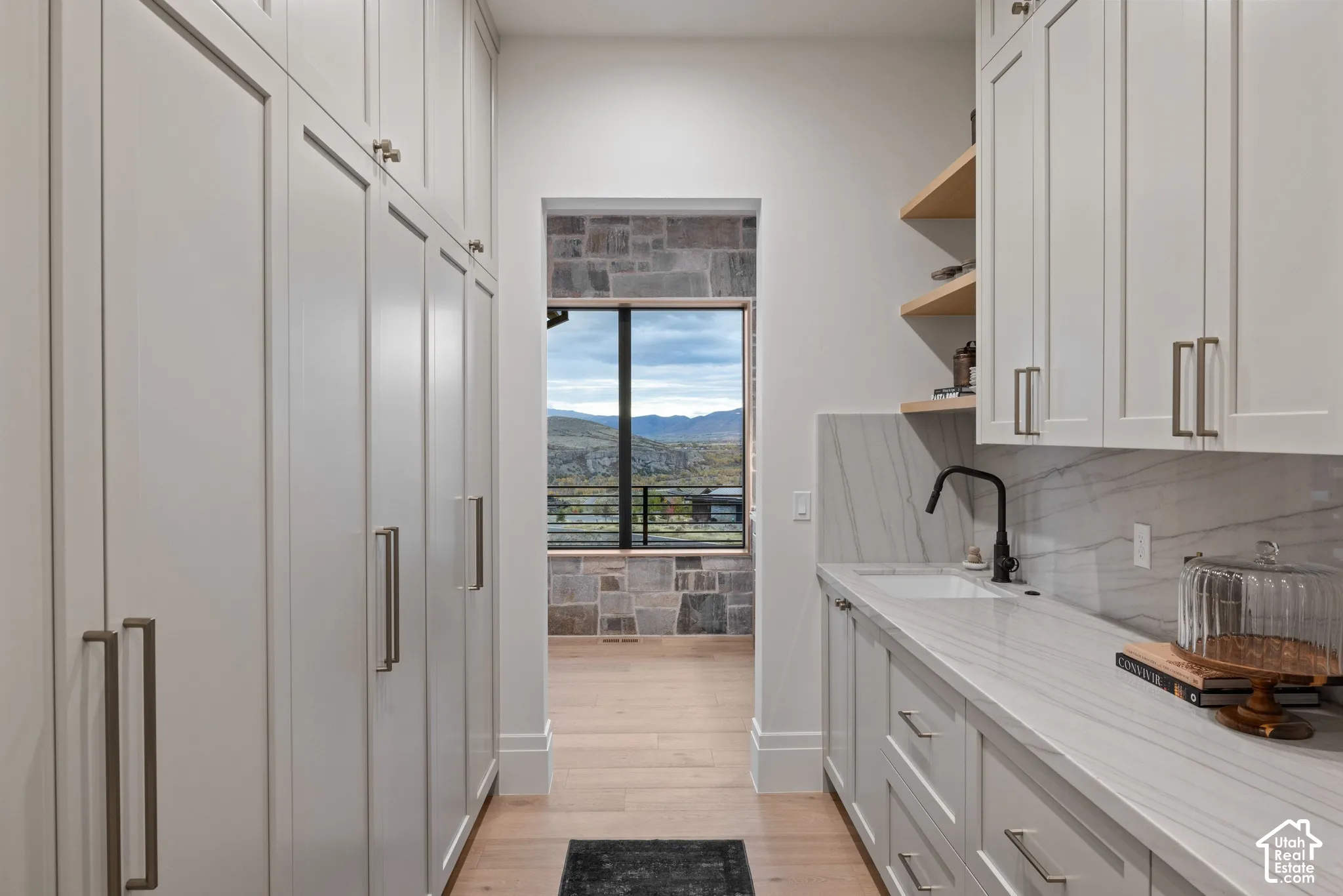 Custom cabinetry with matte finish hardware, stone-patterned backsplash, undermount sink with matte black faucet, wood-finish shelving, and wood-finish flooring