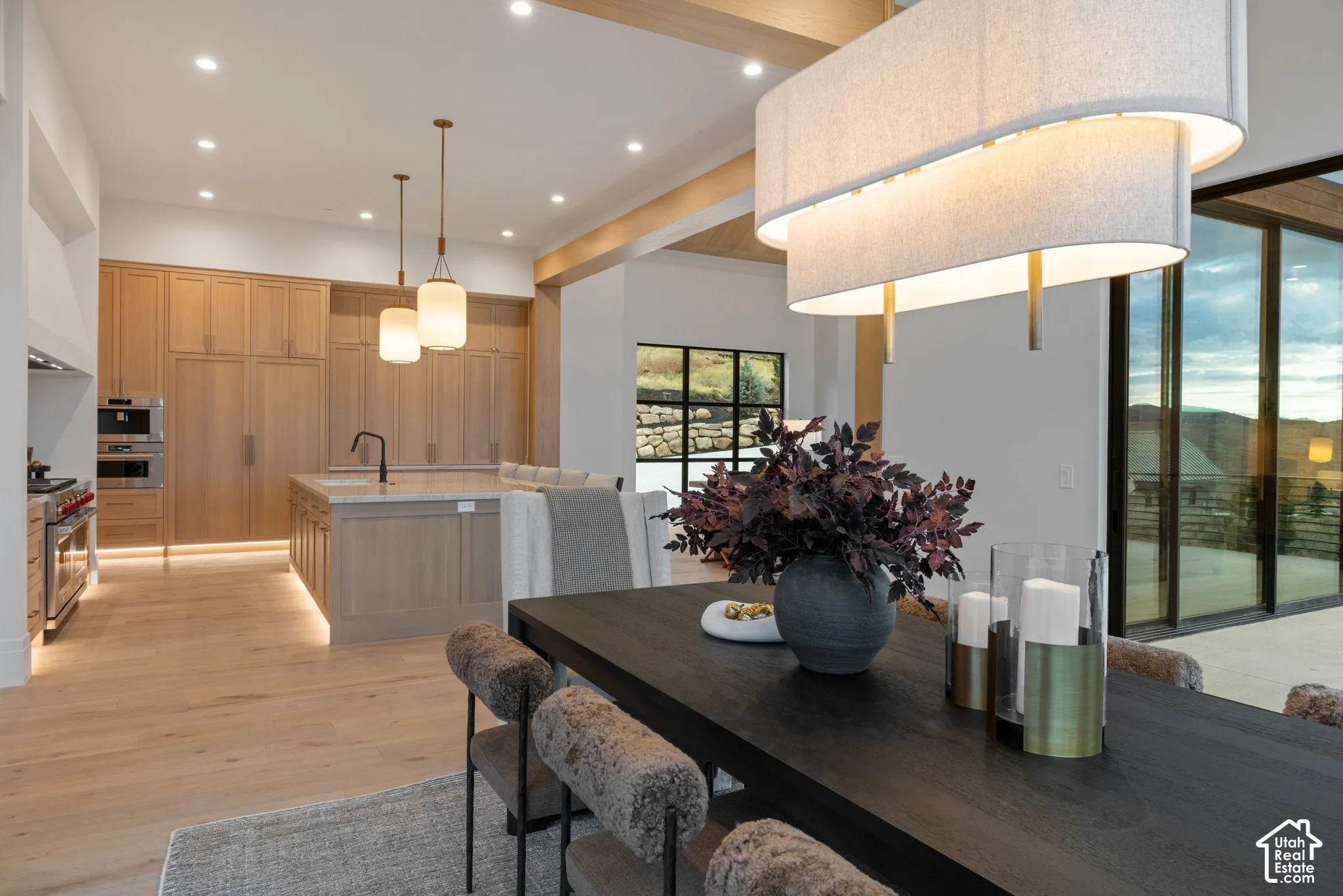 Kitchen featuring custom wood-finish cabinetry, a large central island, recessed ceiling lighting, multi-tiered drum pendant fixture, and expansive floor-to-ceiling glass sliding doors
