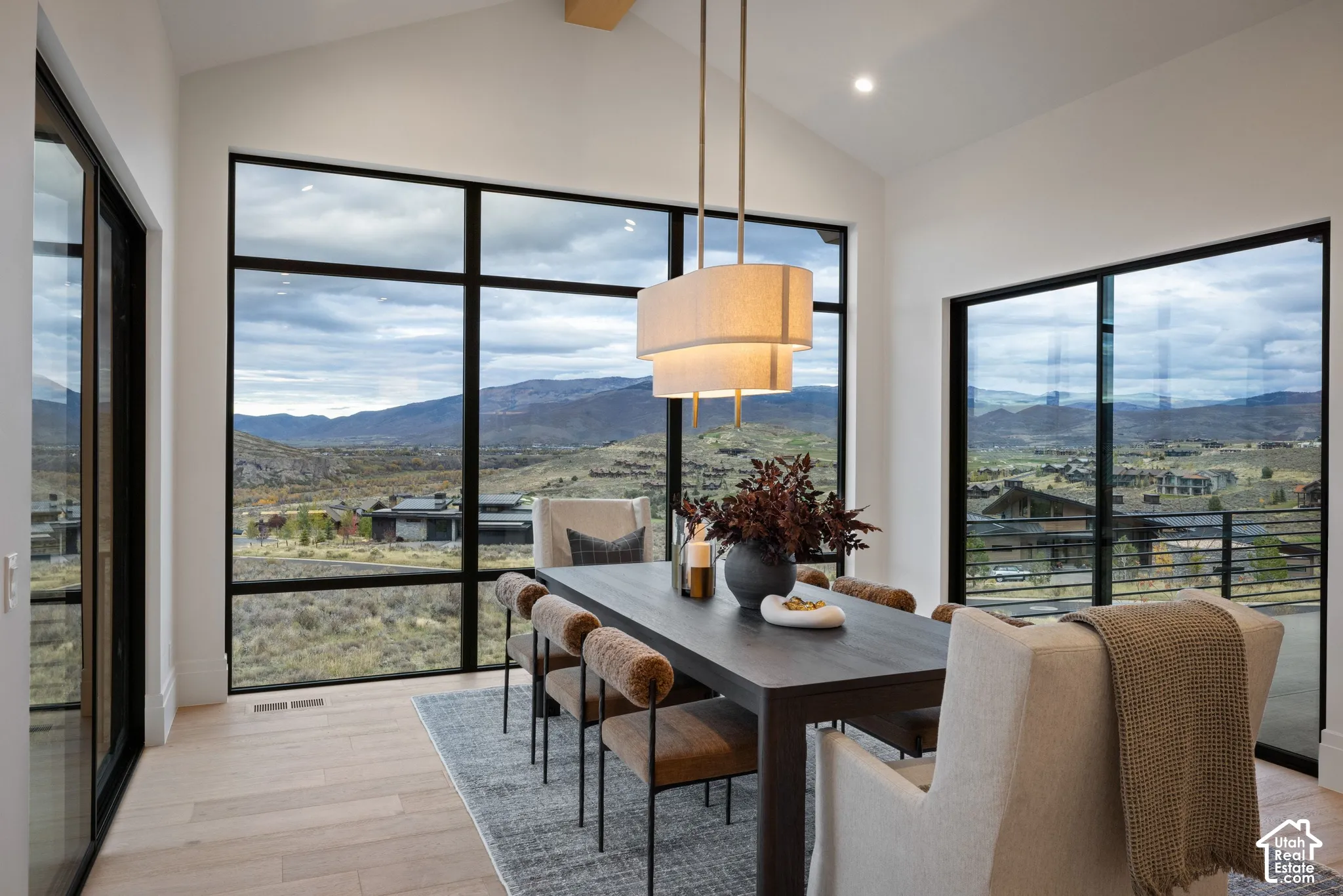 Vaulted ceiling with exposed wood beam, expansive black-framed windows, multi-tiered pendant lighting, and light-tone wood-finish flooring