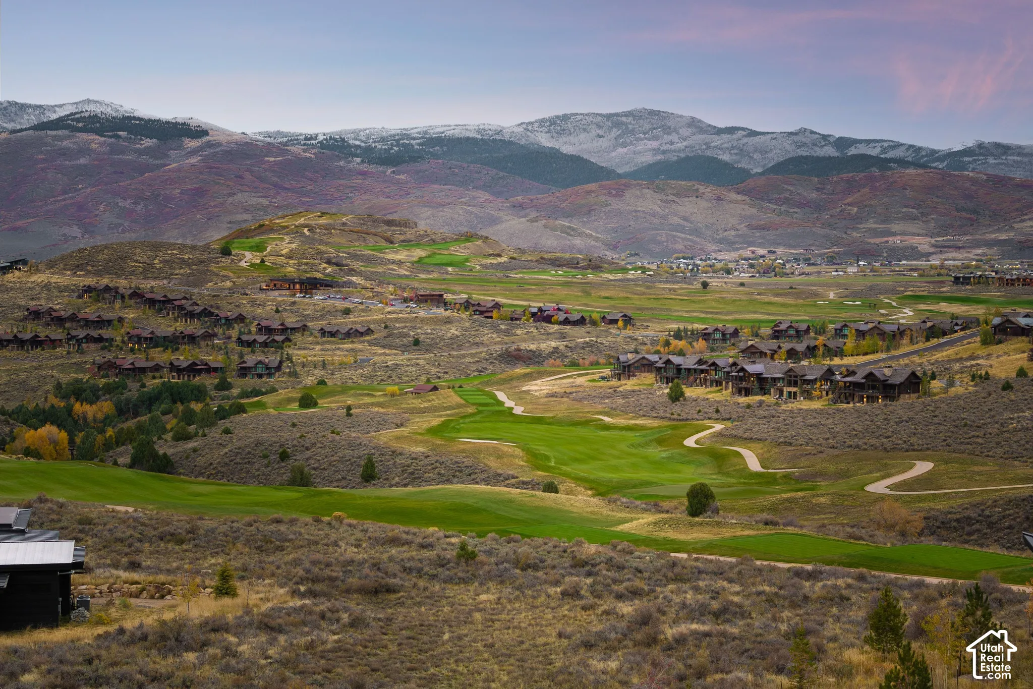 Aerial perspective of mountainous terrain featuring expansive golf course fairways, native high-desert vegetation, and snow-capped peaks