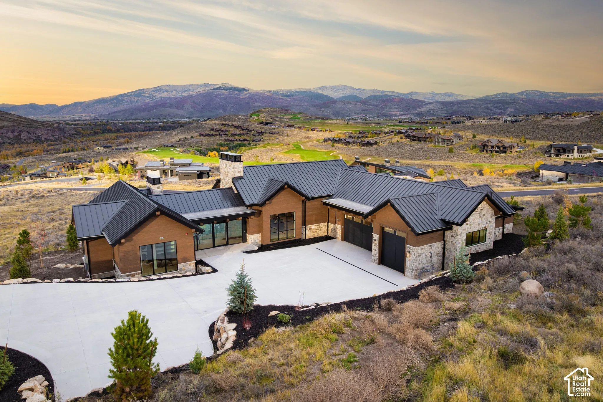 Custom architectural exterior featuring metal roofing, horizontal wood siding, natural stone veneer, a multi-car garage, and expansive mountain scenery