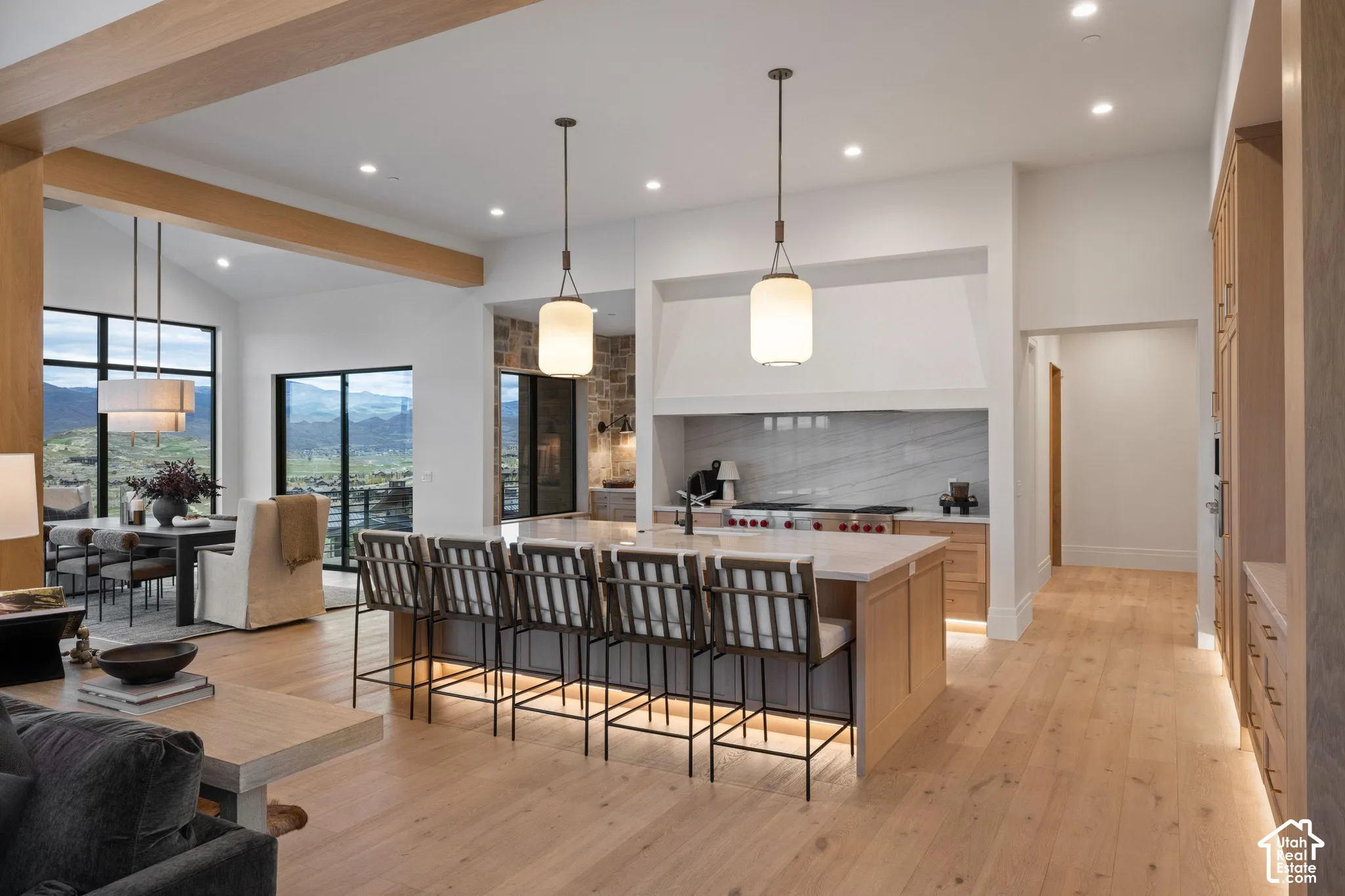 Open-concept kitchen featuring an expansive center island with stone countertops, wood-finish cabinetry, natural stone wall accents, recessed lighting, and dual pendant fixtures