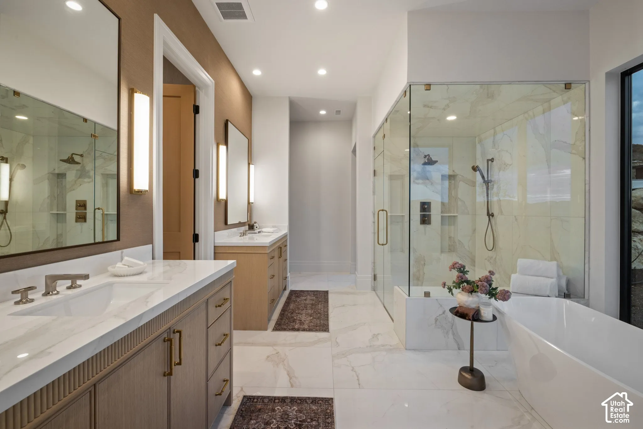 Dual vanities featuring light wood-finish cabinetry, countertop sinks, and wall-mounted lighting