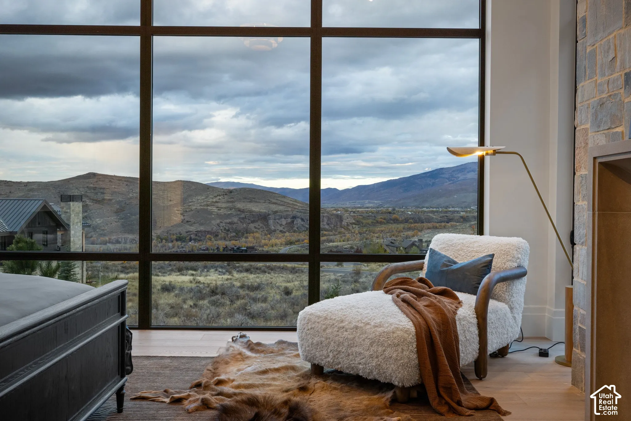 Floor-to-ceiling windows with grid framing, stone-accented wall, and wood-finish flooring, accompanied by expansive mountain scenery
