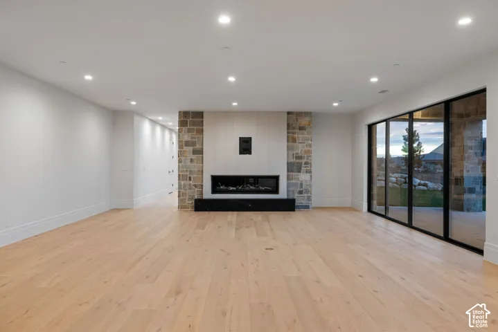 Open-concept interior featuring light wood-finish flooring, recessed lighting, and a floor-to-ceiling stone fireplace surround with a linear hearth