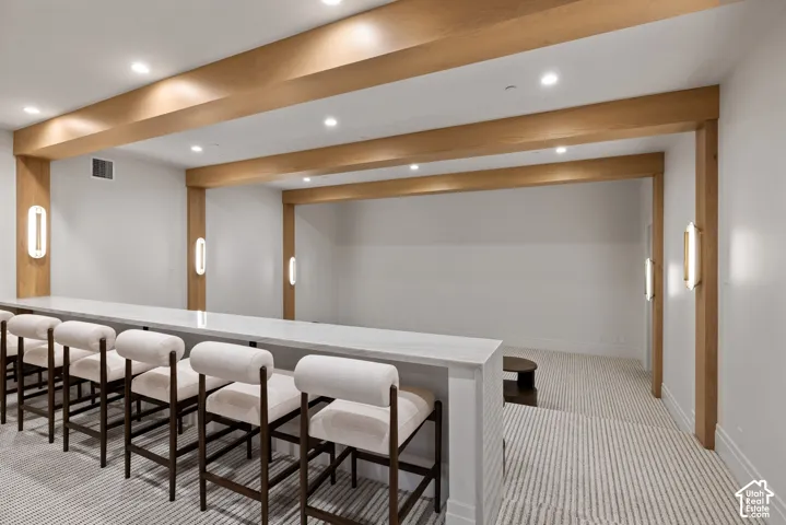 Custom built-in tiered bar with a stone countertop, recessed ceiling lighting, structural natural wood beams, and vertical wall-mounted sconces