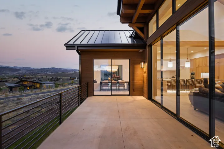 Covered concrete terrace featuring floor-to-ceiling glass sliding doors, dark metal roof, wood-finish siding, and horizontal metal railing
