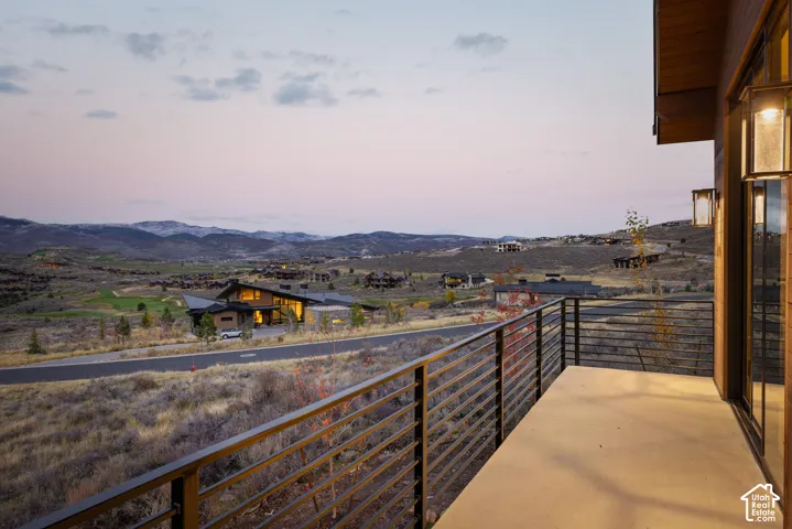 Covered balcony featuring concrete flooring, horizontal metal railing, and wall-mounted exterior lighting, overlooking a mountainous landscape
