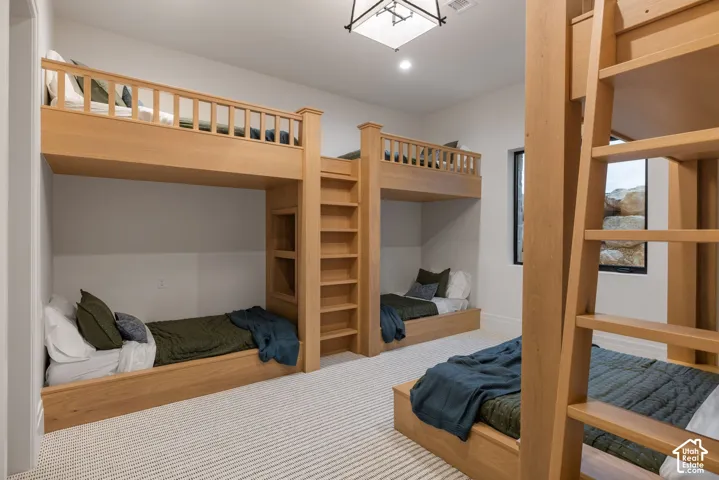 Custom built-in wood-finish bunk beds with integrated shelving and ladders, plush wall-to-wall carpeting, and a geometric pendant light fixture