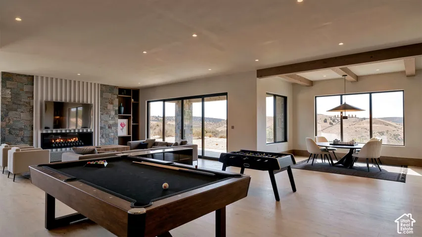 Open-concept living space featuring wood-finish flooring, a linear fireplace with stone masonry surround, recessed lighting, exposed ceiling beams, and large sliding glass doors