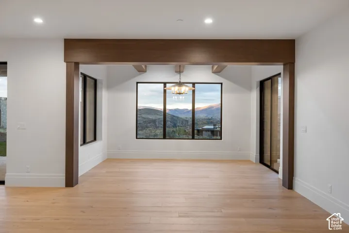 Wood-finish flooring, recessed lighting, exposed ceiling beams, expansive windows with mountain scenery, and metal-framed light fixture