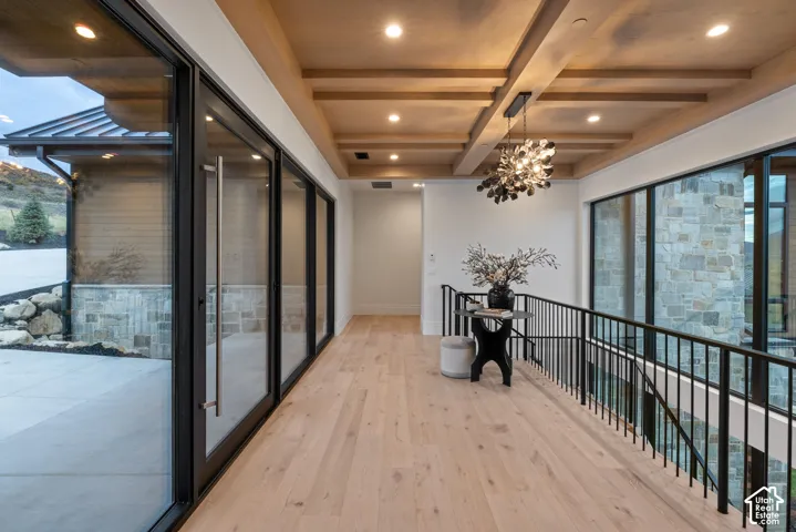 Wood-finish flooring, coffered ceiling with recessed lighting, floor-to-ceiling glass wall, stone exterior masonry, and metal railing with vertical balusters