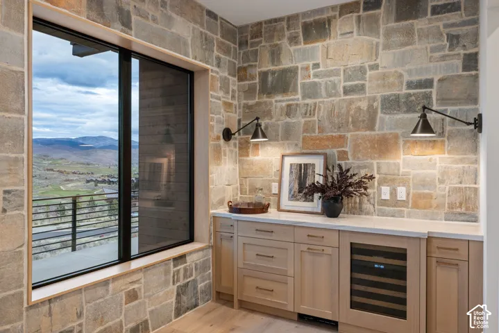 Natural stone wall accents, custom light-toned cabinetry, solid surface countertop, built-in under-counter beverage refrigerator, and dual adjustable wall-mounted sconces