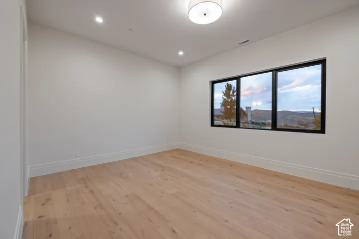 Room featuring wood-finish flooring, minimalist white walls, recessed lighting, a modern drum-style overhead light fixture, and black-framed windows