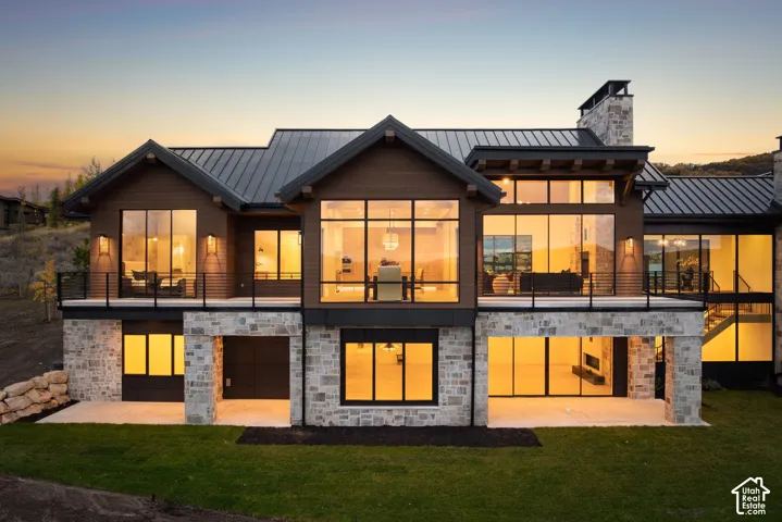 Multi-level architectural exterior featuring dark wood siding, natural stone masonry, a standing-seam metal roof, expansive floor-to-ceiling windows, and an elevated metal-railing deck