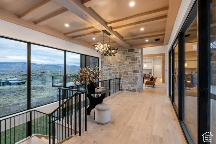 Expansive floor-to-ceiling windows, wood-finish beam ceiling, interior stone accent wall, wood-finish flooring, and metal railing staircase