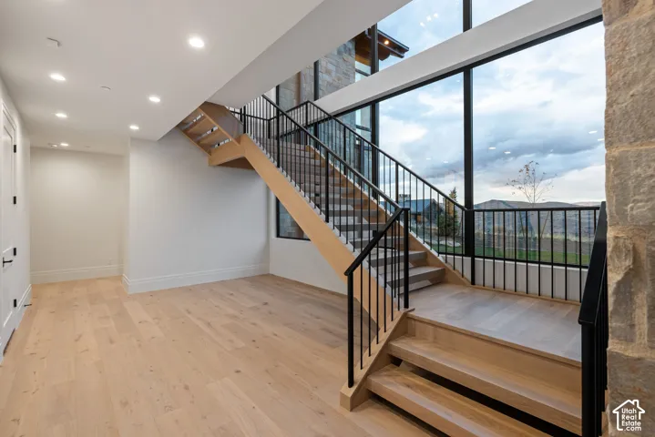 Open staircase featuring wood-finish treads, black metal railing, floor-to-ceiling windows, wood-finish flooring, and natural stone wall accents