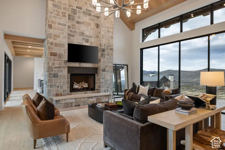 Great room featuring a floor-to-ceiling stone fireplace, vaulted ceiling with wood beams, light wood-finish flooring, large-scale black-framed windows, and a multi-tiered modern chandelier