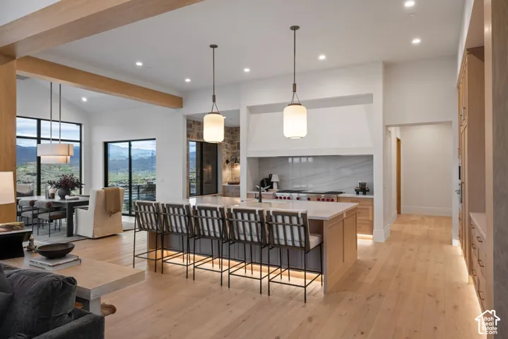 Open-concept kitchen featuring an expansive center island with stone countertops, wood-finish cabinetry, natural stone wall accents, recessed lighting, and dual pendant fixtures