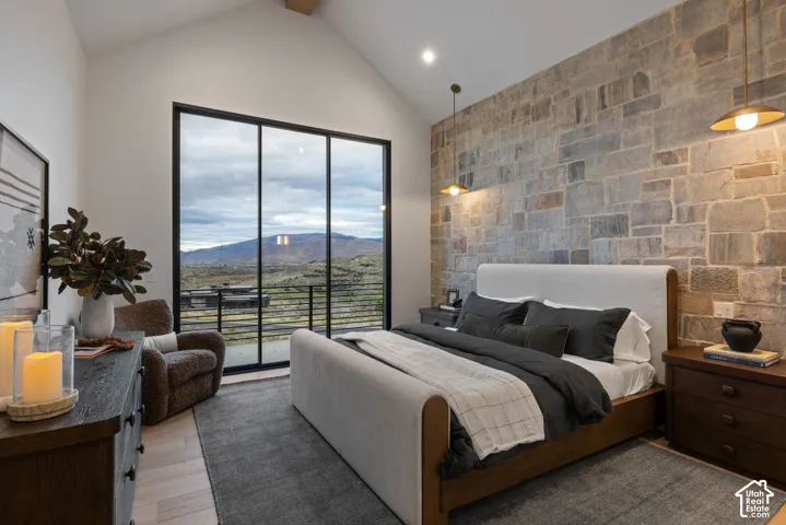 Vaulted ceiling, full-height masonry accent wall, floor-to-ceiling glass sliding doors, wood-finish flooring, and recessed lighting