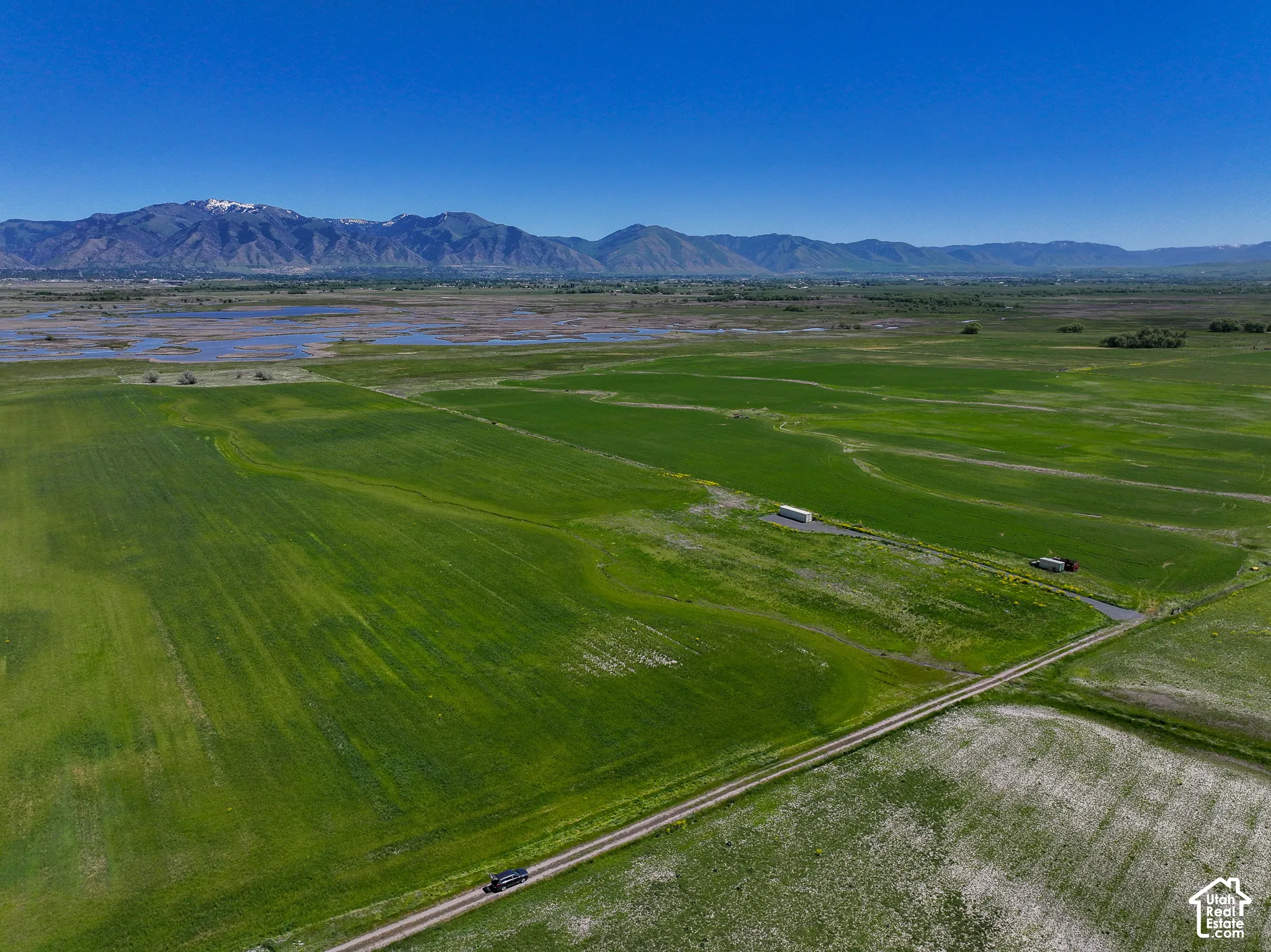 Expansive acreage featuring open green fields, a gravel access road, and mountain range backdrop