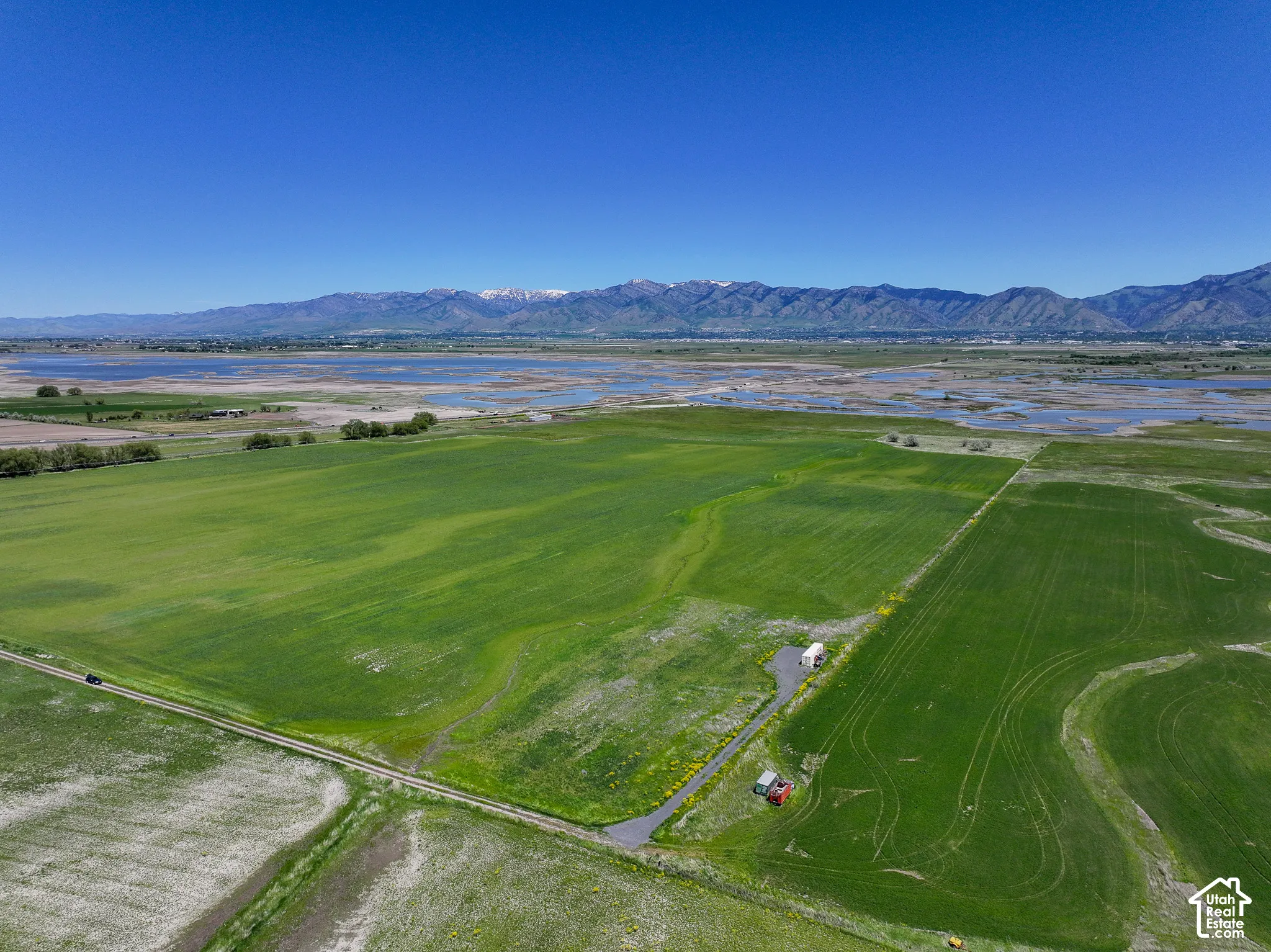 Expansive parcel featuring level agricultural land, a paved access road, and prominent mountain and water scenery