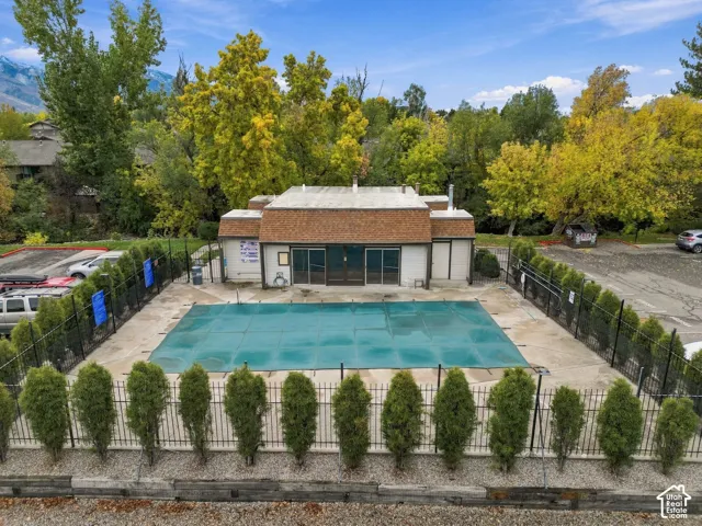 Swimming pool with protective cover, fenced perimeter, mature tree landscaping, and single-story structure with shingled roof