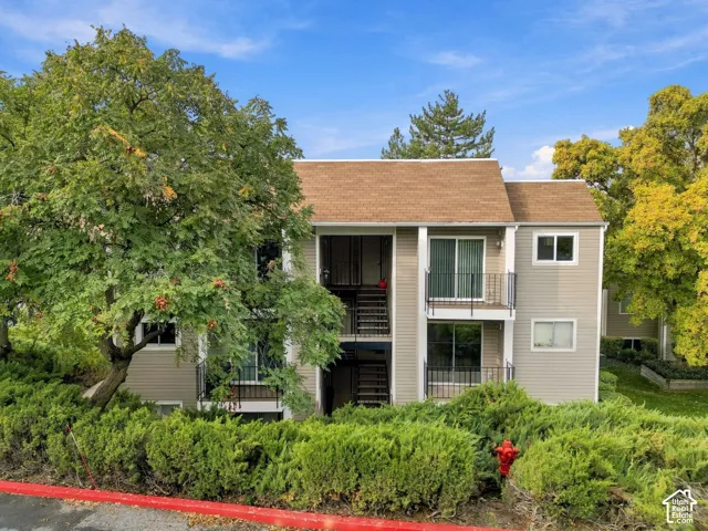 Multi-story exterior with neutral siding, shingled roofing, stacked private balconies with black metal railings, and mature landscaping