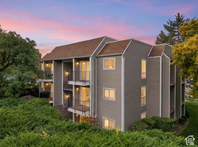 Multi-level exterior featuring horizontal siding, a shingled mansard roof, private metal-railed balconies, and mature landscaping