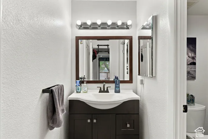Dark wood-finish vanity with an integrated white sink, topped by a framed mirror, a multi-bulb vanity light fixture, and a wall-mounted matte black towel bar