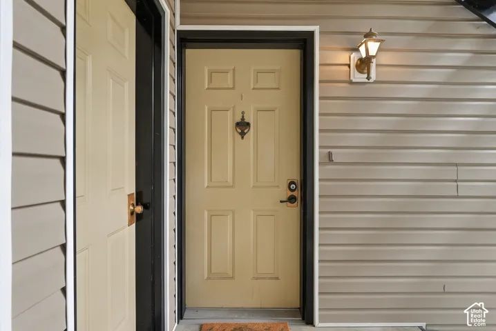 Exterior entrance featuring horizontal vinyl siding, a six-panel door with a mounted door knocker, and an attached wall-mounted lantern-style light fixture